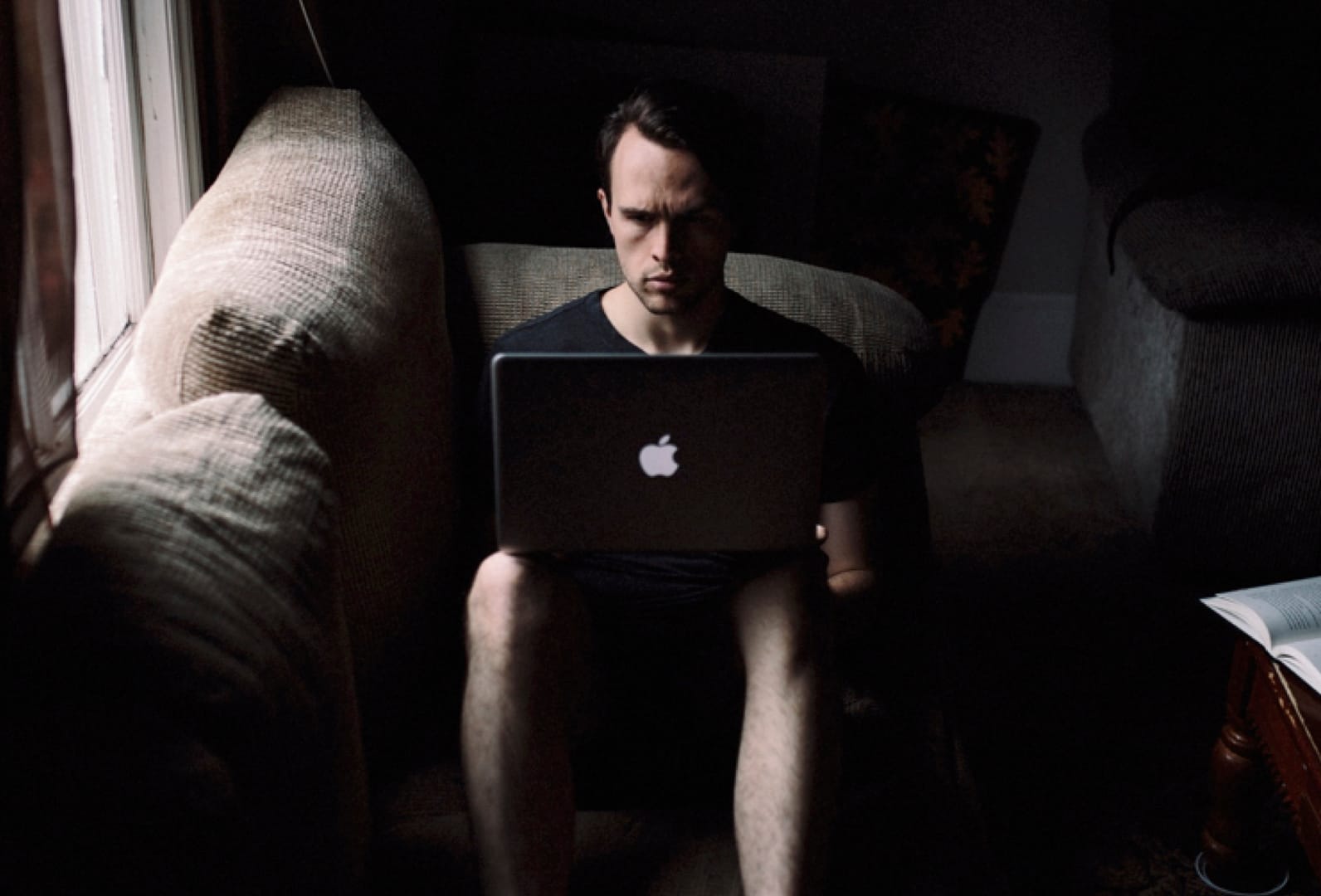 A young man sitting on a couch intensely engaged with his laptop