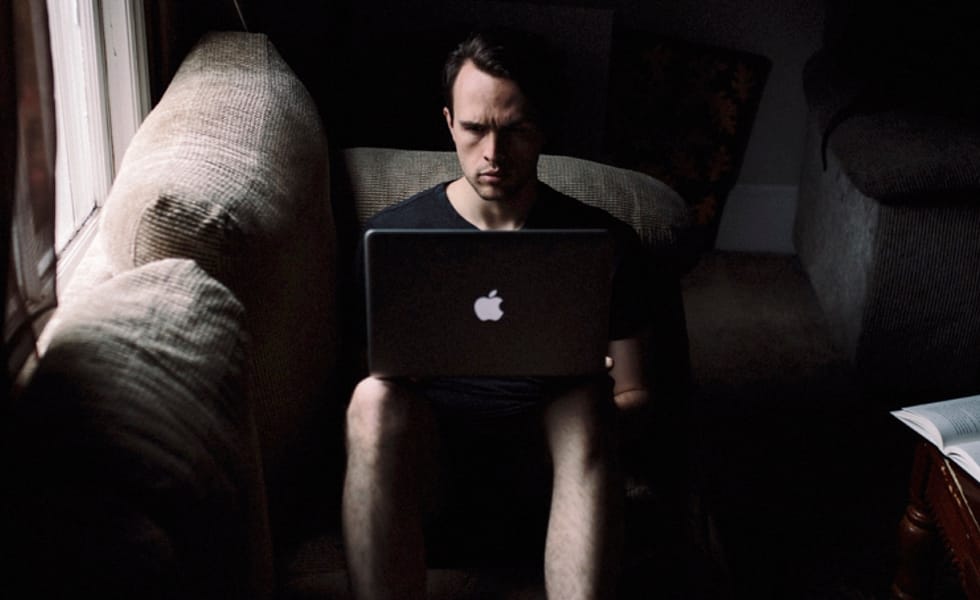 A young man sitting on a couch intensely engaged with his laptop