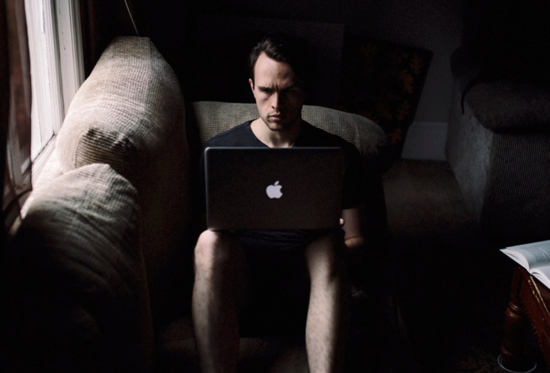 A young man sitting on a couch intensely engaged with his laptop